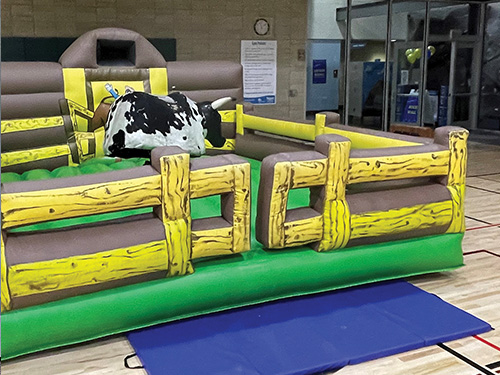 A green and yellow inflatable surrounds a white and black mechanical bull.