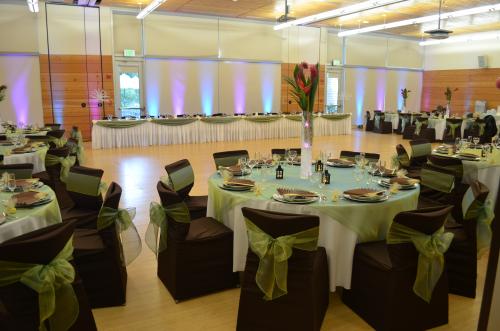 A ballroom is set with one long table and may round tables all decorated in brown and green for a formal event.
