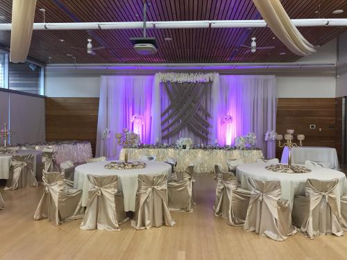 A ballroom with round tables and chairs decorated for a formal event with shades of purple and gold.