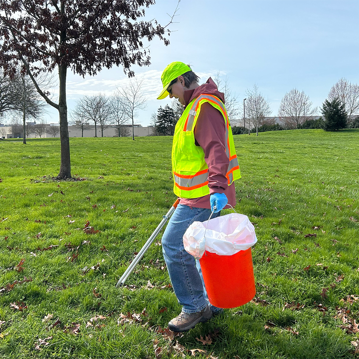 Volunteer picking up litter at local park with field and tree in background