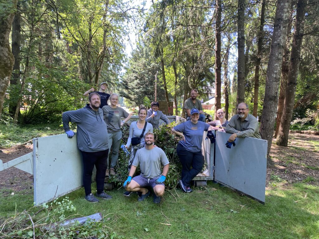 group of volunteers poses near open dumpster filled with ivy