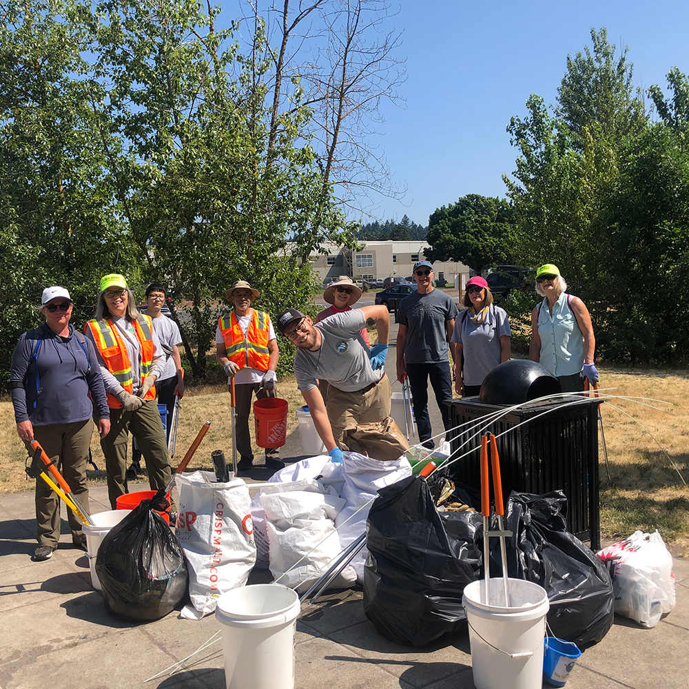 Volunteers smile with bags of garbage collected on a sunny cleanup