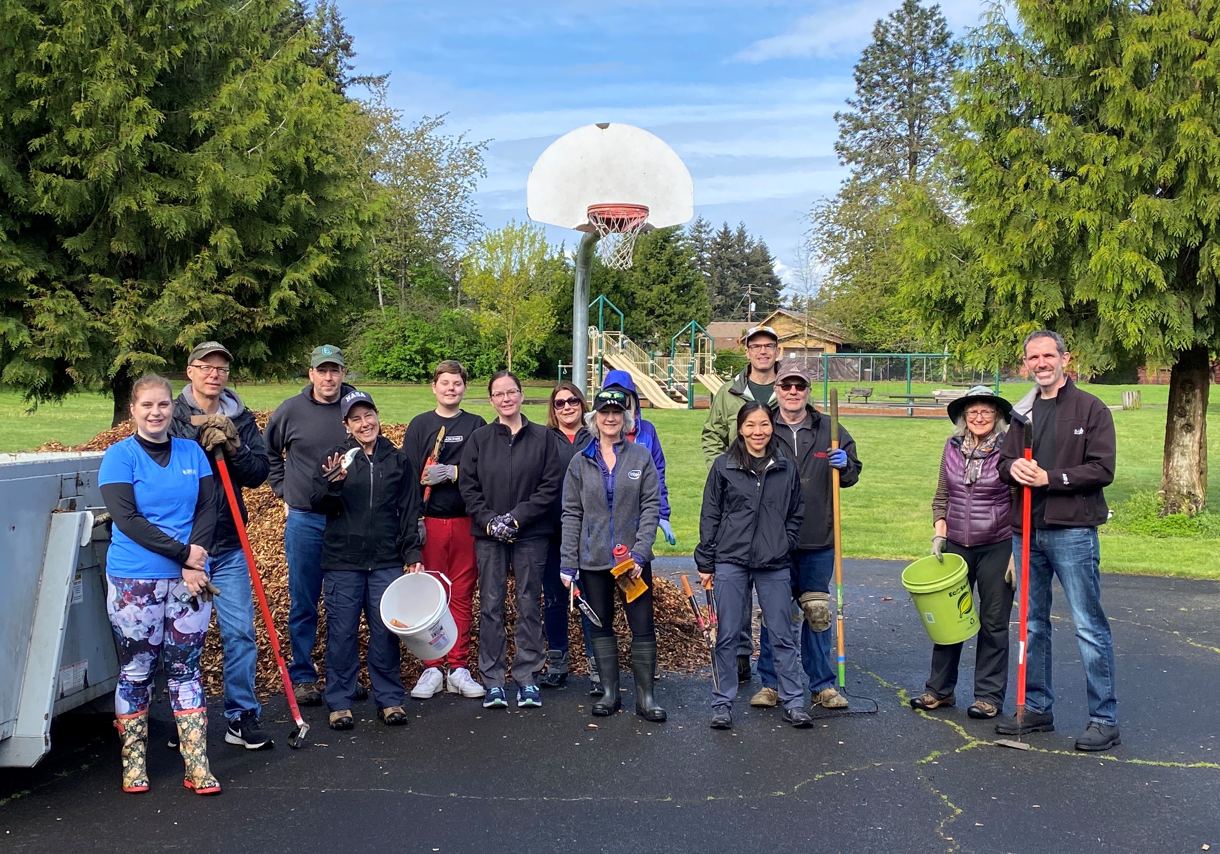 group of volunteers poses holding tools near a dropbox on a basketball court in a park