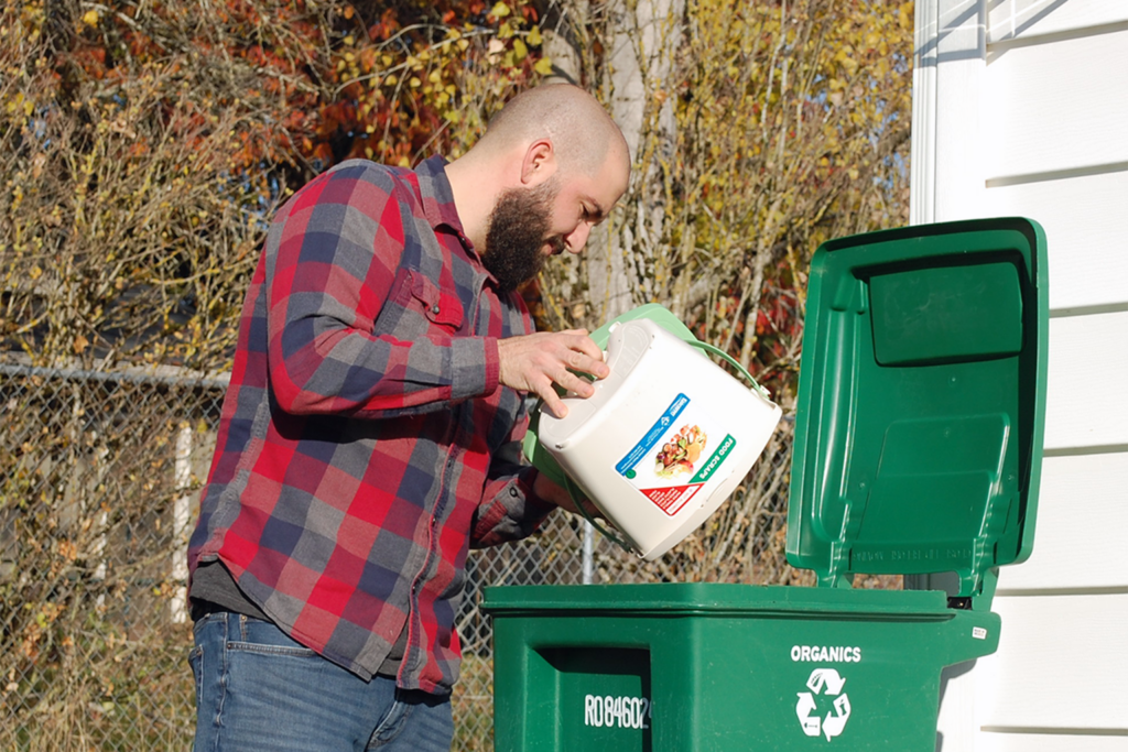 Man empties a compost bin into an organics cart