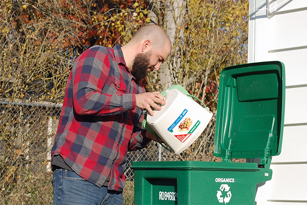 Man empties a compost bin into an organics cart