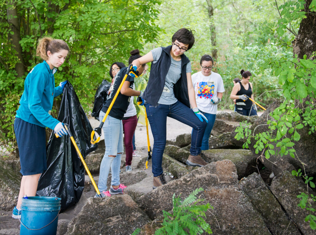 five volunteers using litter grabbers to pick up trash in the woods