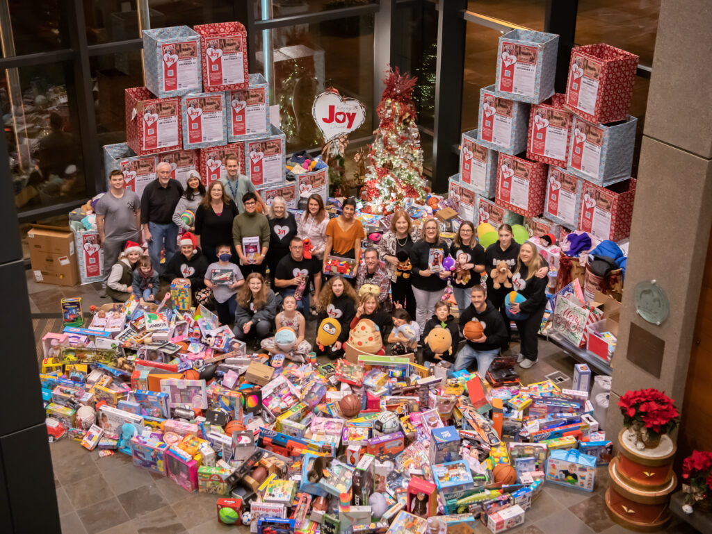 A group of city employees stand in the middle of a large pile of gifts collected during the 2023 Joy Drive. 