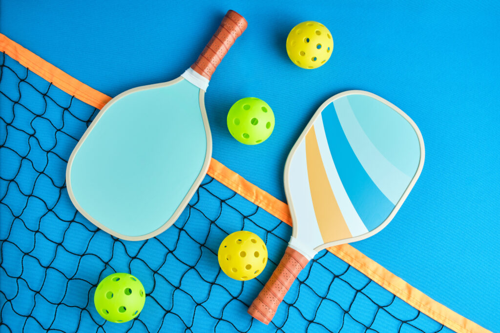 Two pickleball paddles and four balls on top of a net on blue background