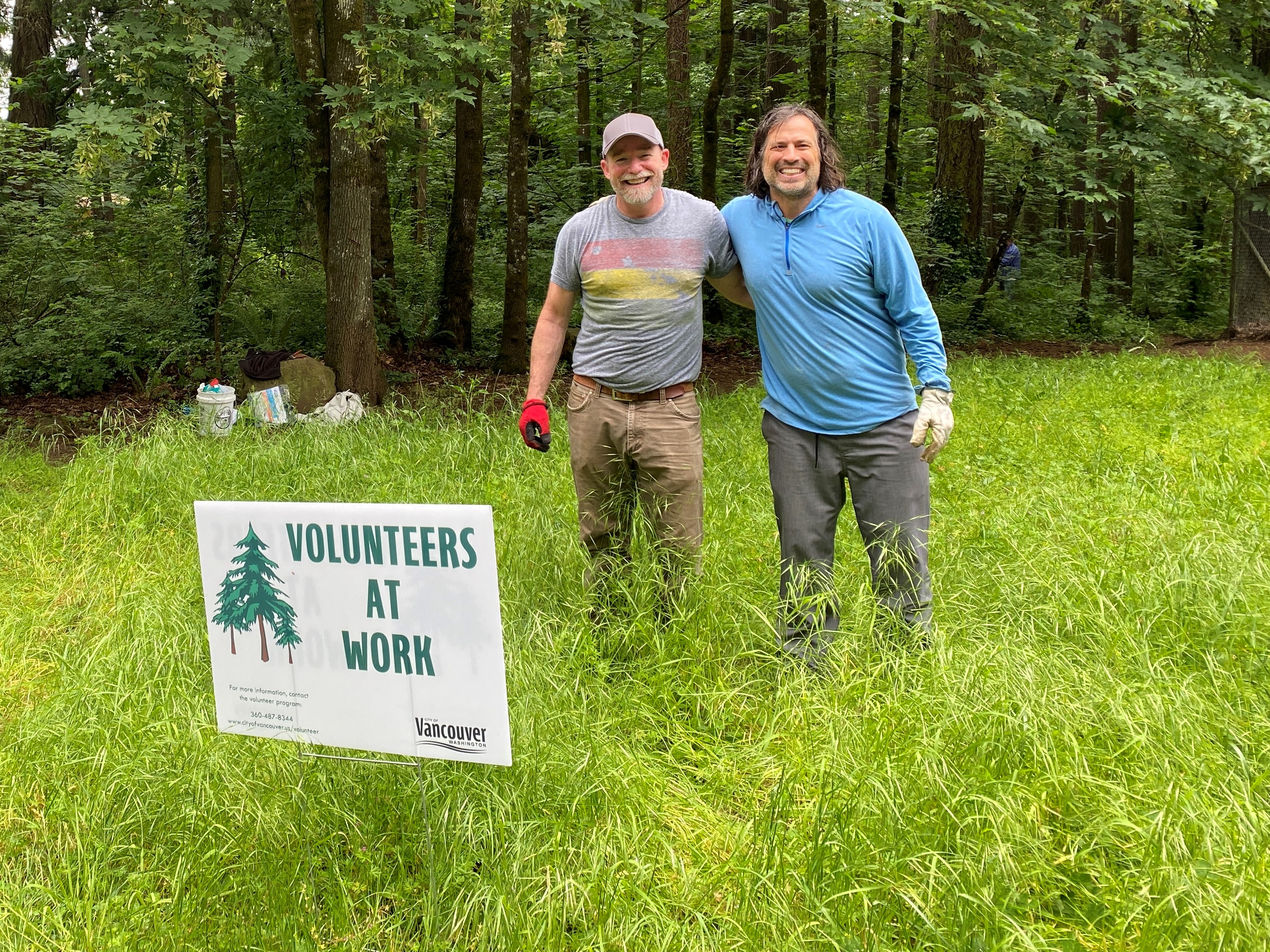 two volunteers stand in a field with a sign that reads 