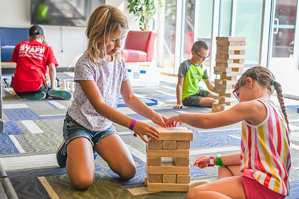 Two young day camp participants build a large Jenga tower together.