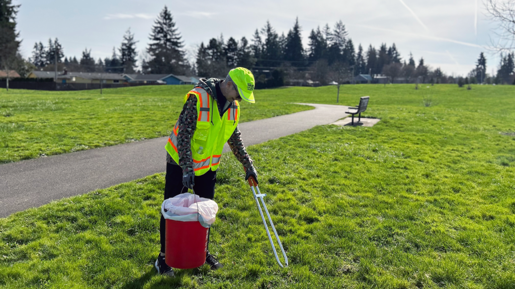 Volunteer picking up litter at local park with path and bench in background