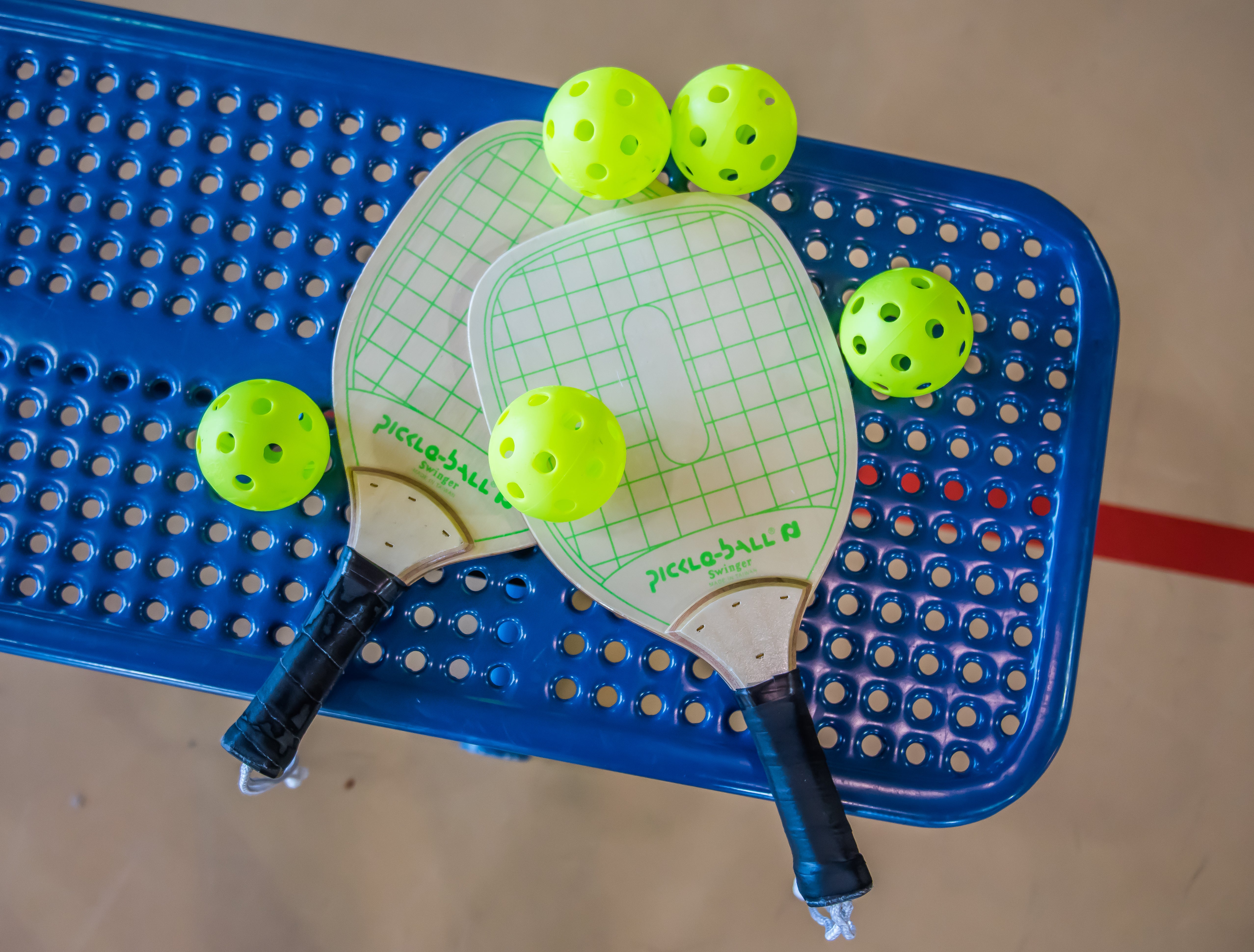 Pickleball paddles and balls on a blue gym bench