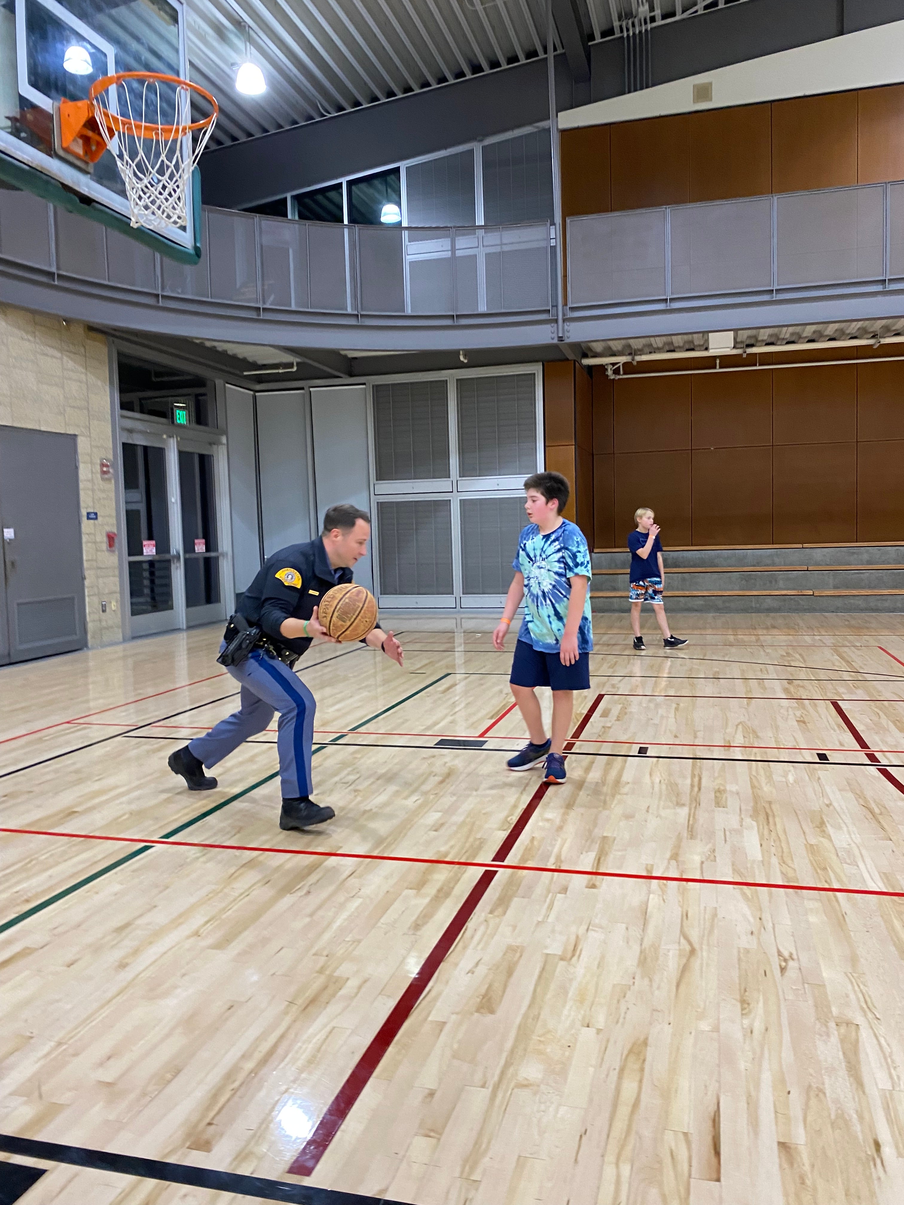 Police officer and teen play basketball in the Firstenburg Gymnasium