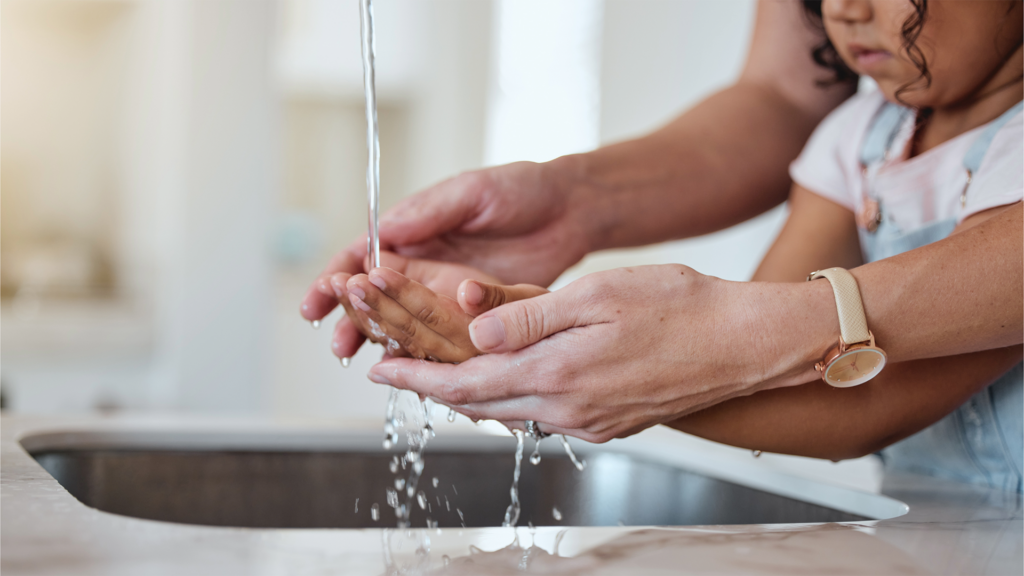 Adult and child using stream of water at sink to wash hands